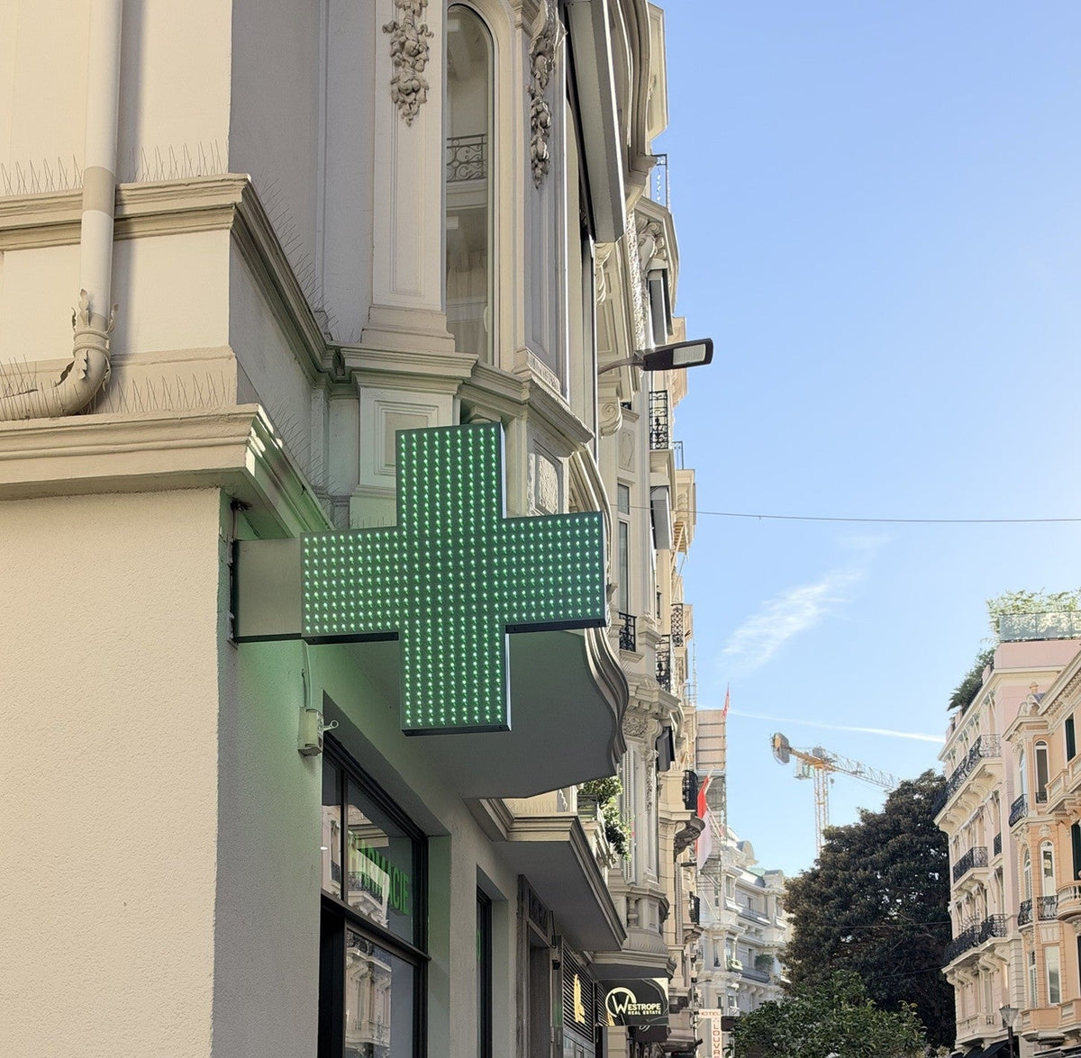 Pharmacy green cross sign on a Monaco street lined with Belle Époque buildings