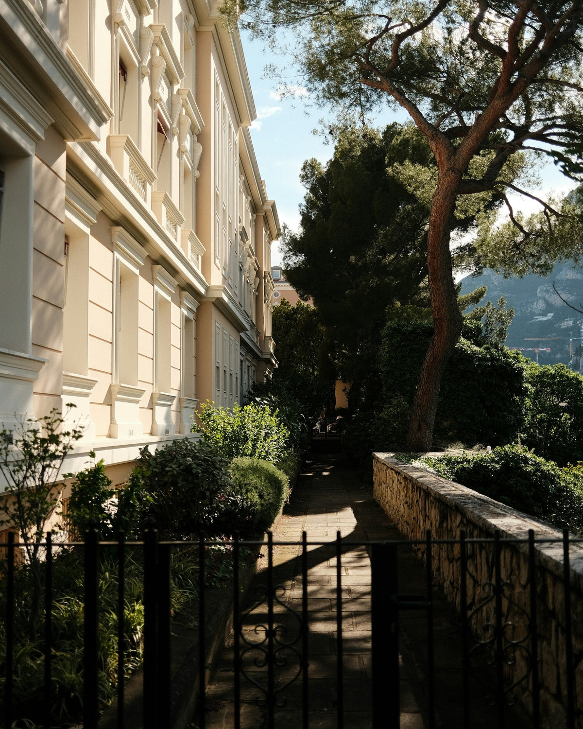 Quiet residential lane beside a Belle Epoque apartment building in Monaco, with pine trees and an iron gate