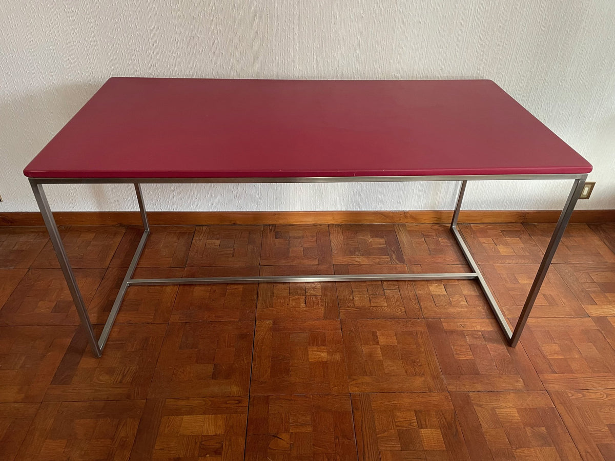 Ghyslaine de Freijo desk with raspberry-red top on a brushed stainless steel frame, three-quarter view