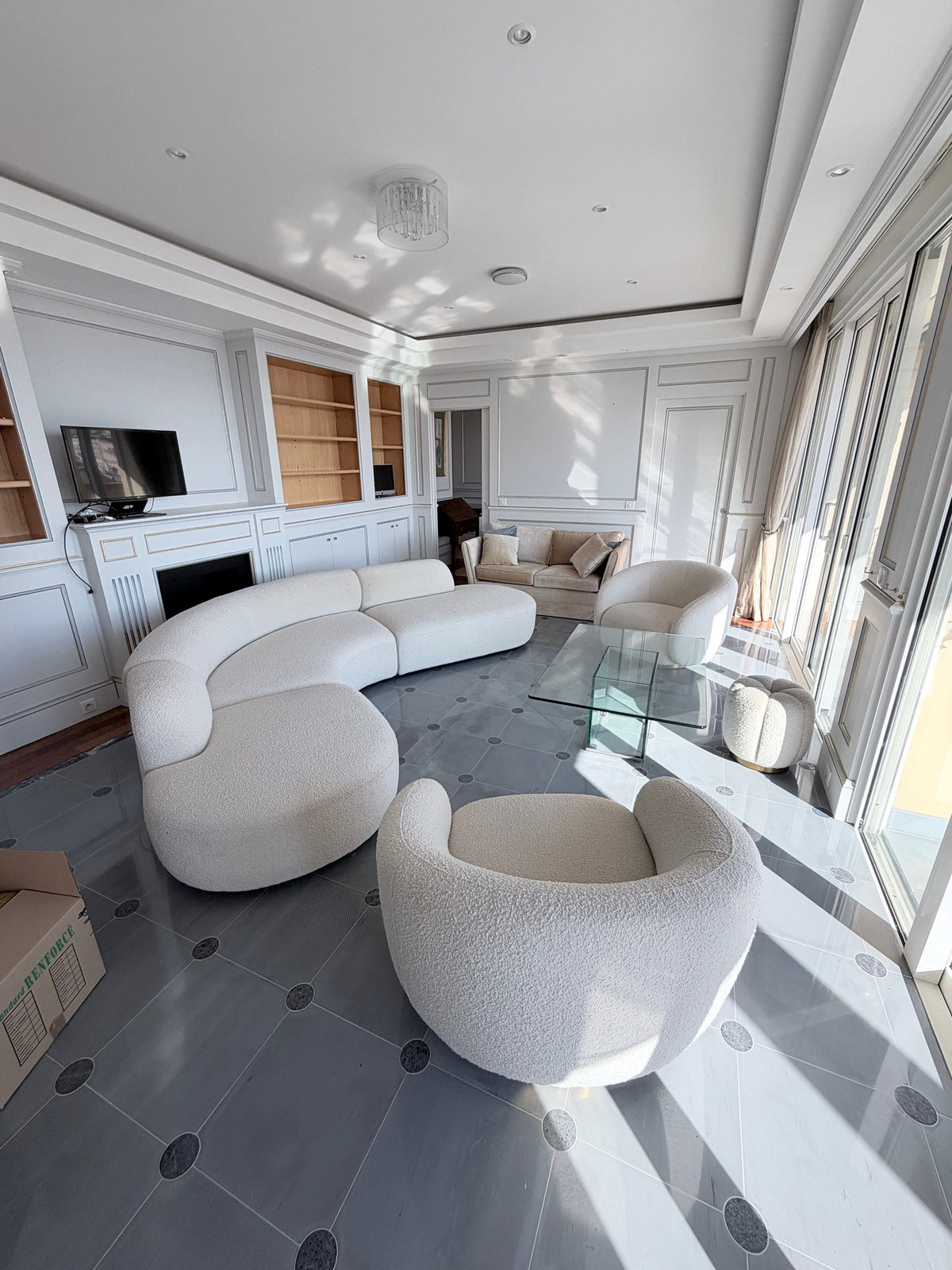 Bright Monaco apartment living room with a curved bouclé sofa, armchairs and a moving box, on moving-in day