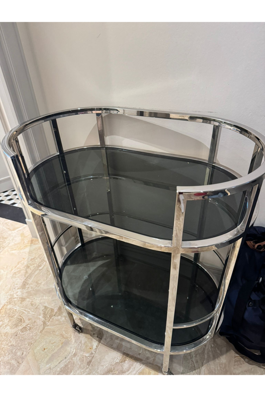 Chrome and smoked glass bar cart by Anastasia Tarutova featuring a sleek drinks trolley with desserts on top.